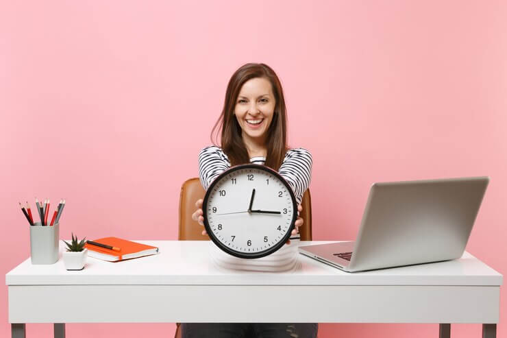 Smiling-woman-holding-round-alarm-clock-while-sit-working-project-white-desk-with-contemporary-pc-laptop-isolated-pastel-pink-background-achievement-business-career-concept-copy-space 365776-10933